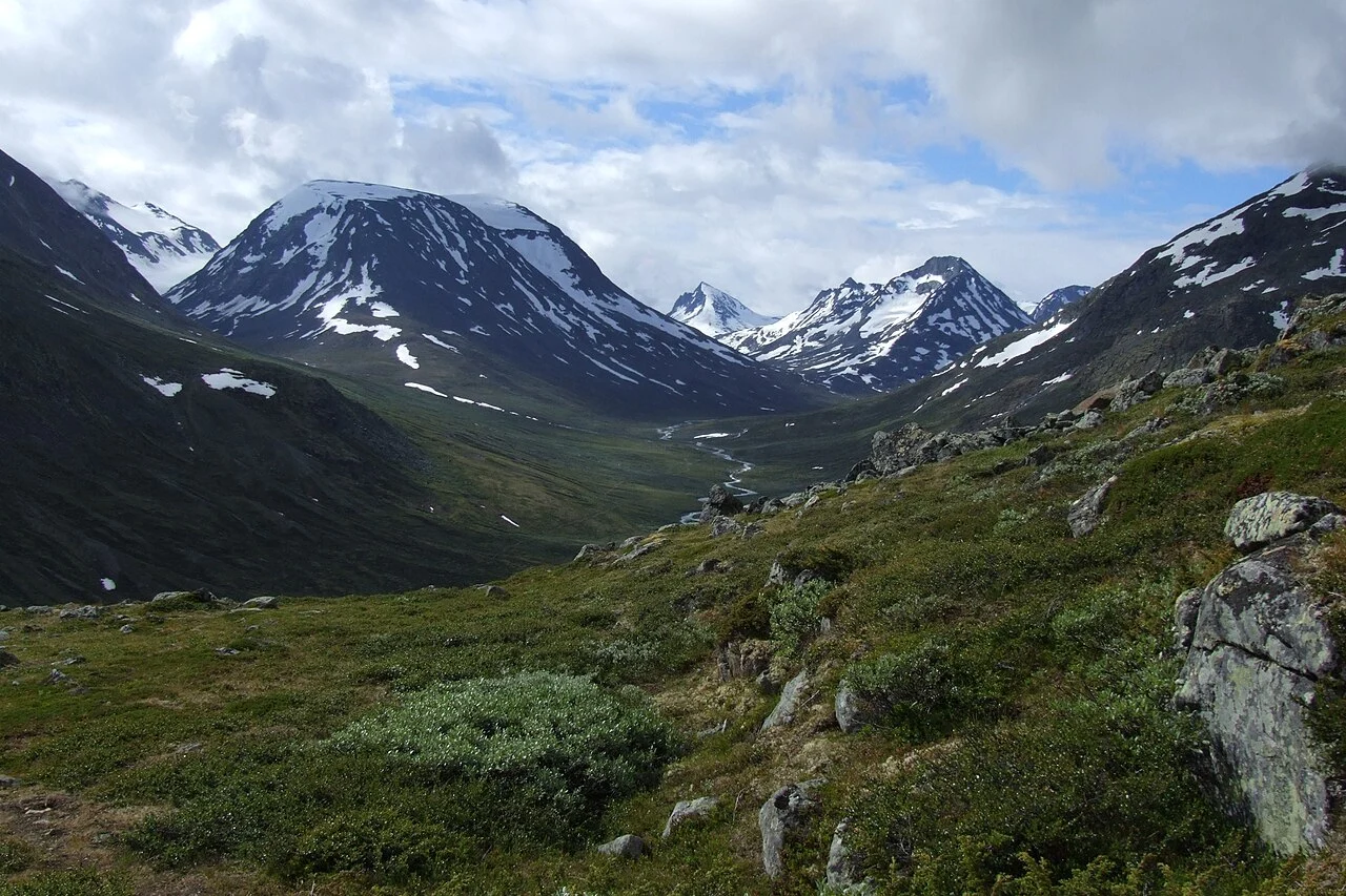 Fjeldlandskab i Jotunheimen i Norge med dal, elv og sneklædte toppe